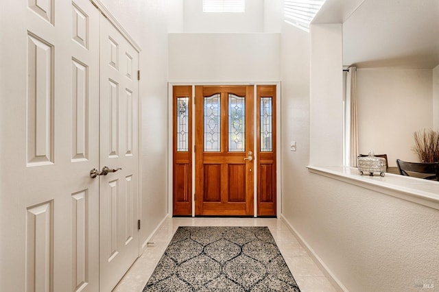 entrance foyer with light tile patterned flooring, baseboards, and a towering ceiling