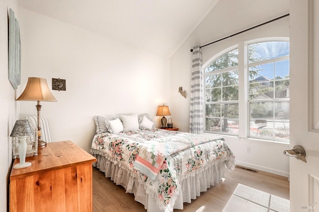 bedroom featuring visible vents, baseboards, light wood finished floors, and lofted ceiling