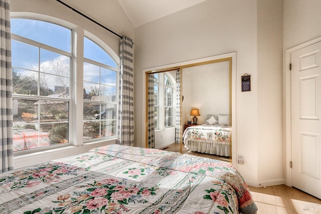 bedroom with baseboards, wood finished floors, a closet, and vaulted ceiling