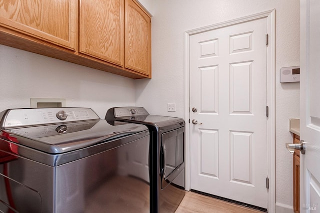laundry room with cabinet space, washer and dryer, and light wood-style floors