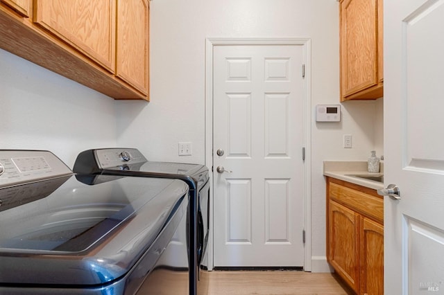 clothes washing area featuring cabinet space, light wood-style flooring, and washing machine and dryer