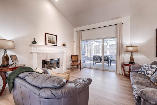 living area featuring light wood-style floors, high vaulted ceiling, and a tiled fireplace
