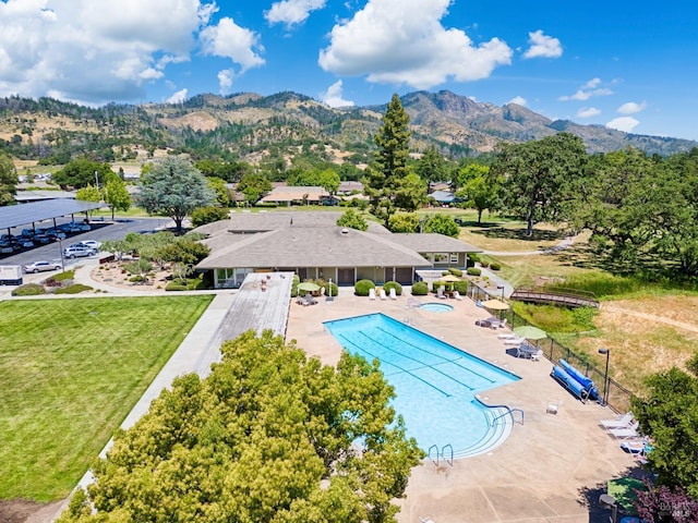 community pool with a patio, a yard, a mountain view, and fence