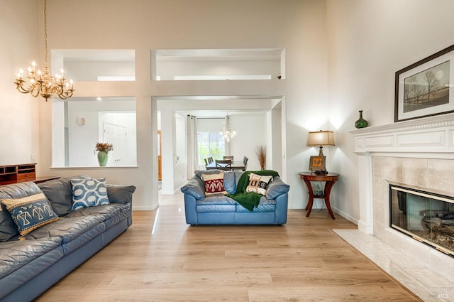 living room featuring a tiled fireplace, a high ceiling, light wood-type flooring, and an inviting chandelier