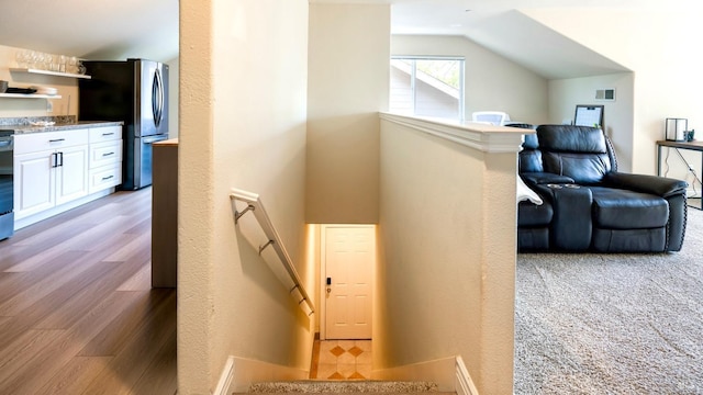 hallway featuring wood finished floors, vaulted ceiling, and an upstairs landing