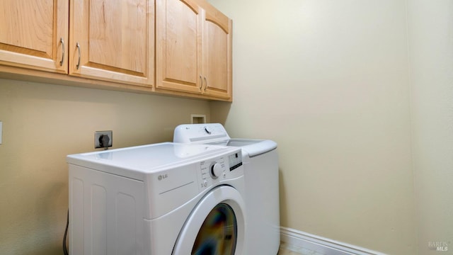 clothes washing area with baseboards, washing machine and dryer, and cabinet space