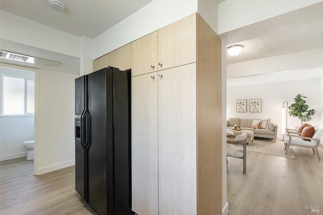 kitchen with light brown cabinets, baseboards, a textured ceiling, black refrigerator with ice dispenser, and light wood finished floors