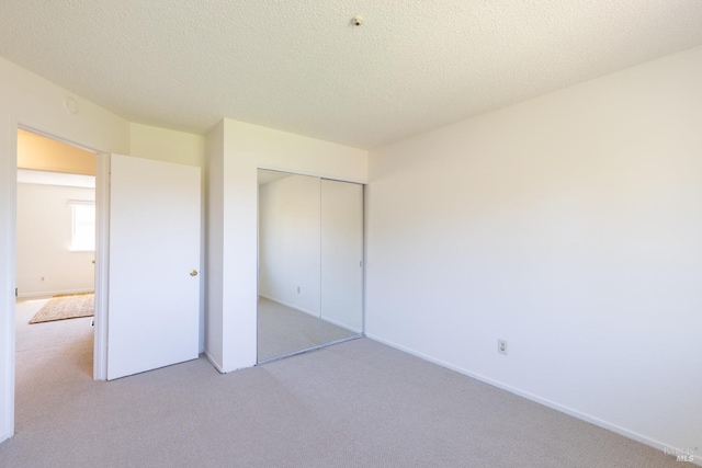 unfurnished bedroom featuring light carpet, baseboards, a closet, and a textured ceiling