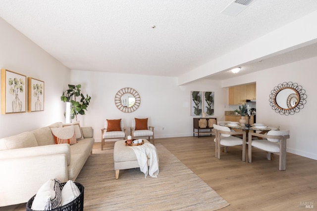 living room featuring light wood-style flooring, a textured ceiling, baseboards, and visible vents