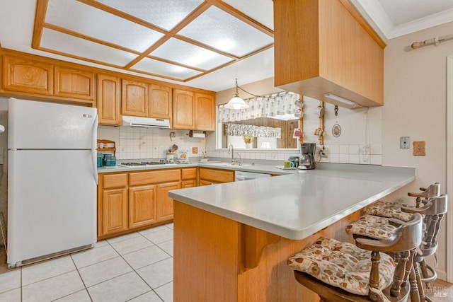 kitchen featuring ornamental molding, white appliances, a peninsula, under cabinet range hood, and backsplash