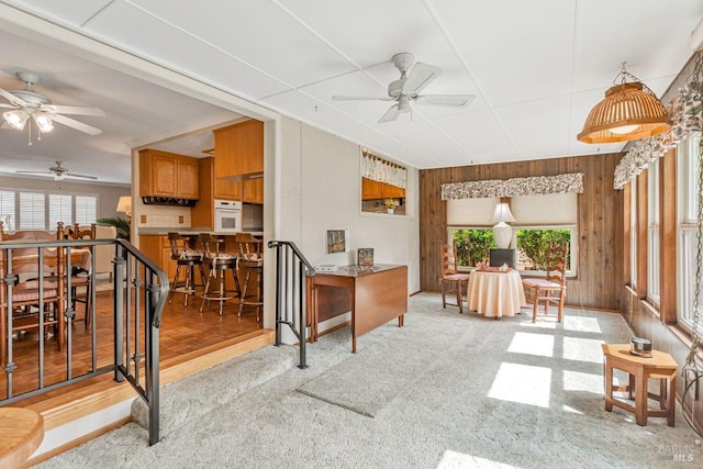 interior space with oven, a ceiling fan, brown cabinets, wood walls, and light colored carpet
