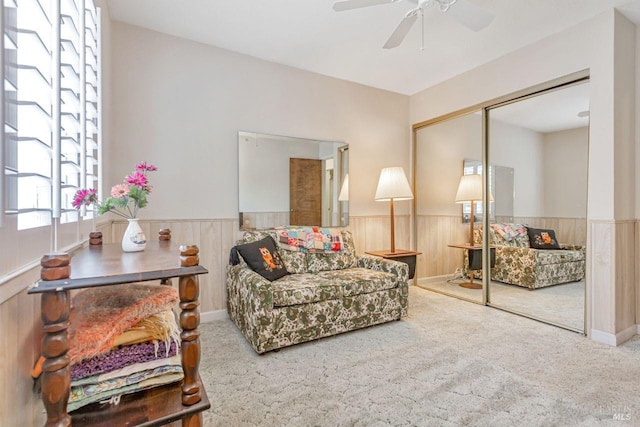 carpeted living area featuring a ceiling fan, wooden walls, and wainscoting