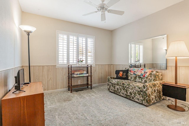living area featuring wood walls, ceiling fan, and wainscoting