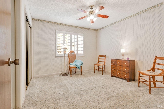 sitting room featuring a textured ceiling, wallpapered walls, a ceiling fan, and carpet floors