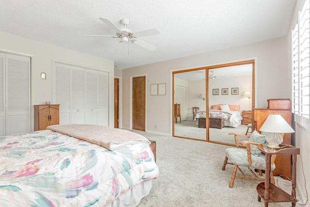 carpeted bedroom with baseboards, a textured ceiling, two closets, and ceiling fan
