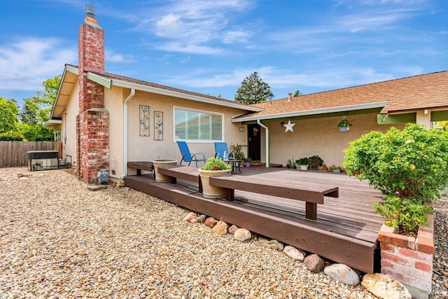 rear view of house featuring fence, stucco siding, a deck, and a chimney