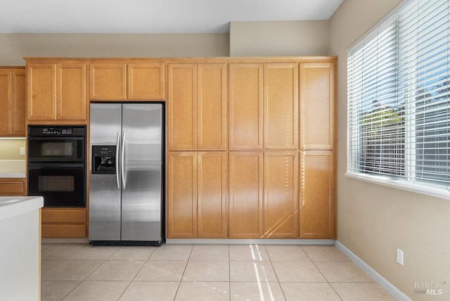 kitchen with dobule oven black, stainless steel fridge with ice dispenser, light tile patterned floors, light countertops, and baseboards