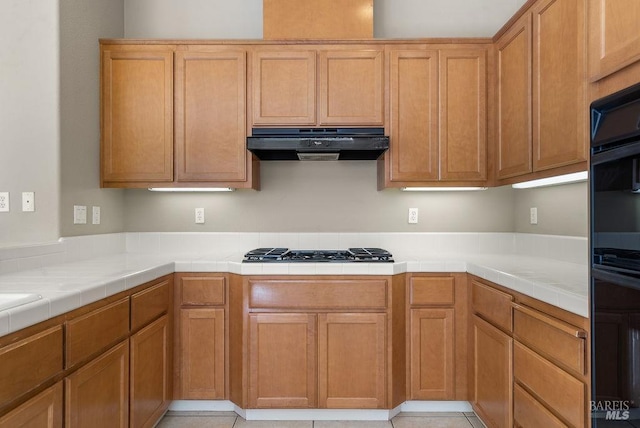 kitchen featuring under cabinet range hood, black gas stovetop, and tile counters