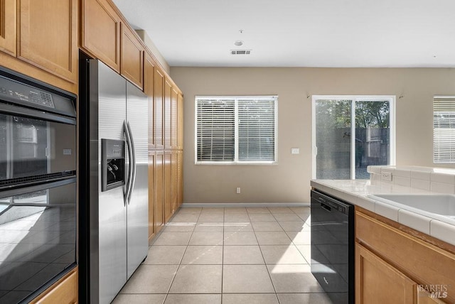 kitchen with baseboards, tile counters, light tile patterned floors, visible vents, and black appliances