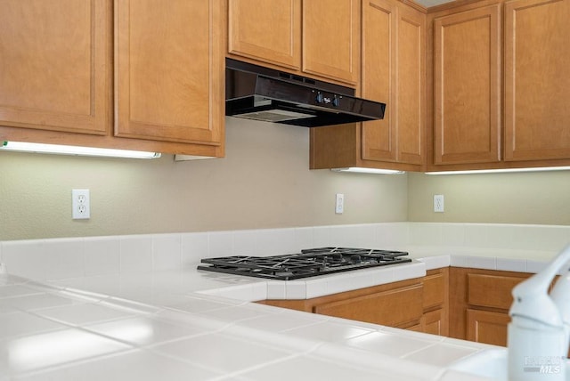 kitchen with tile countertops, gas stovetop, and under cabinet range hood