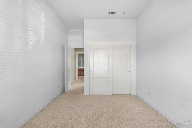 unfurnished bedroom with light carpet, visible vents, a closet, and baseboards