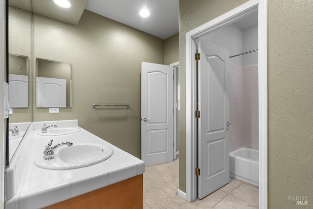 bathroom with a textured wall, shower / bath combination, double vanity, and a sink