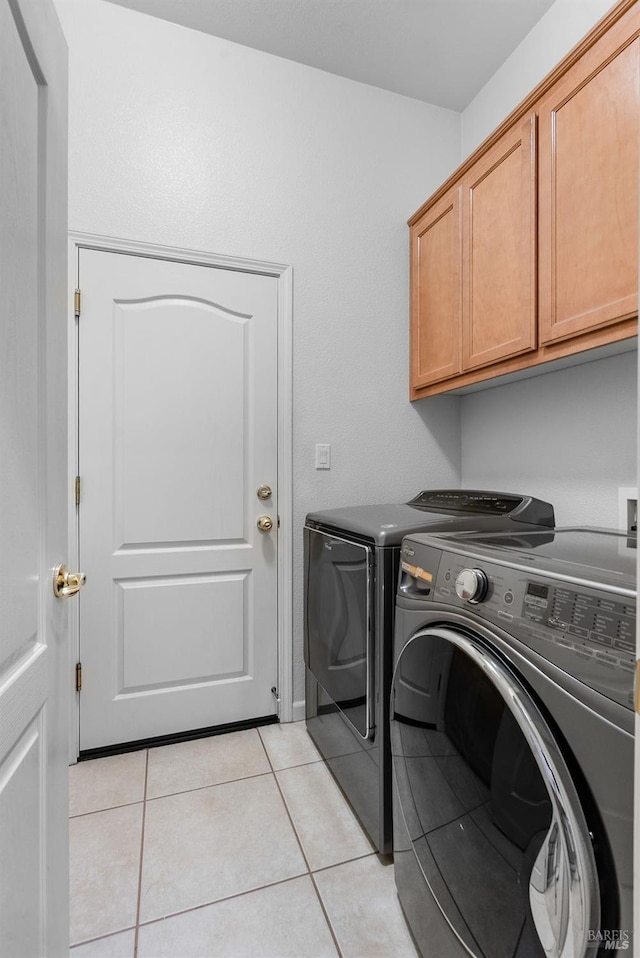 laundry area featuring washing machine and clothes dryer, cabinet space, and light tile patterned floors