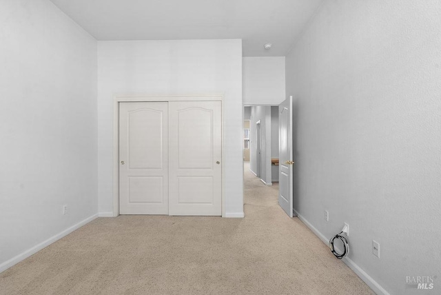 unfurnished bedroom with a closet, light colored carpet, and baseboards