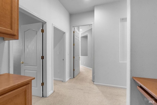 corridor with baseboards and light colored carpet