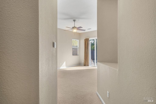 hall with a textured wall, visible vents, baseboards, and carpet floors