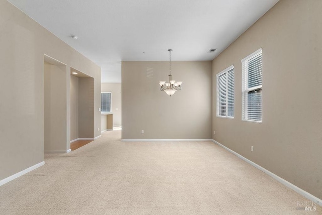 carpeted empty room with visible vents, baseboards, and a notable chandelier