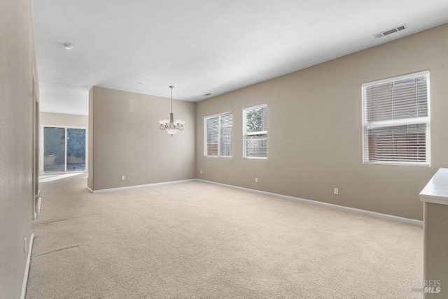 empty room featuring light colored carpet, an inviting chandelier, baseboards, and visible vents