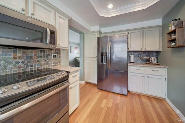 kitchen with ornamental molding, light wood-style flooring, open shelves, a tray ceiling, and stainless steel appliances