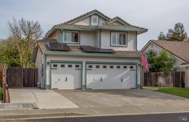 view of front facade featuring roof mounted solar panels, a garage, a tile roof, fence, and driveway