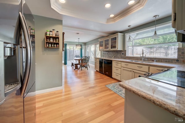 kitchen with a sink, a tray ceiling, light wood-type flooring, and stainless steel fridge