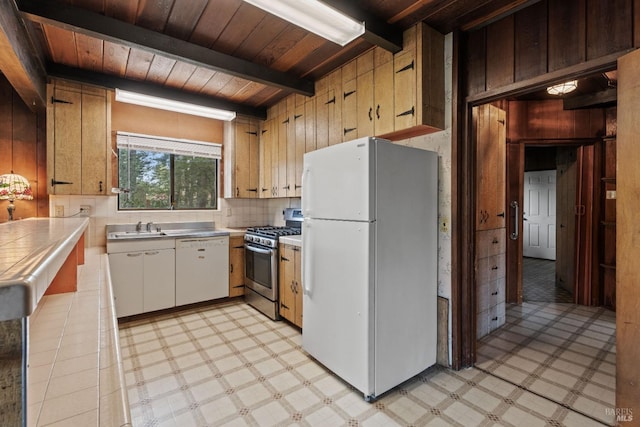 kitchen featuring wooden walls, stainless steel counters, white appliances, and light floors
