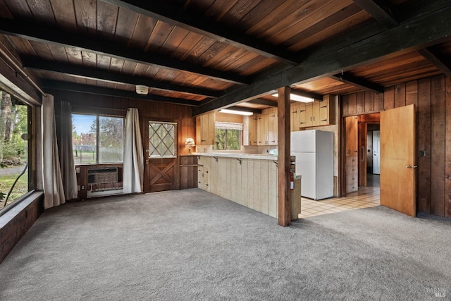 kitchen with light countertops, freestanding refrigerator, wood walls, beam ceiling, and light colored carpet