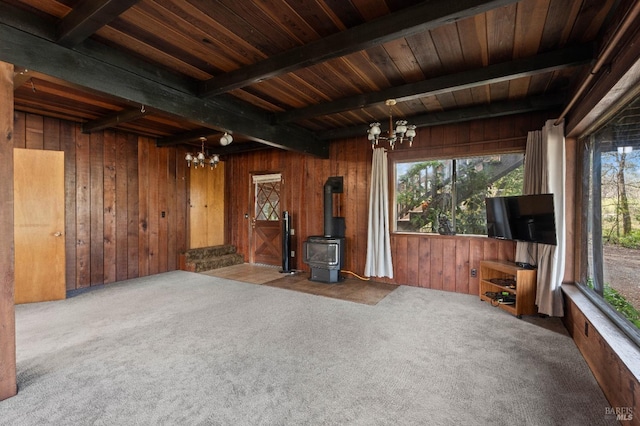 unfurnished living room with a chandelier, a wood stove, wooden walls, and beam ceiling