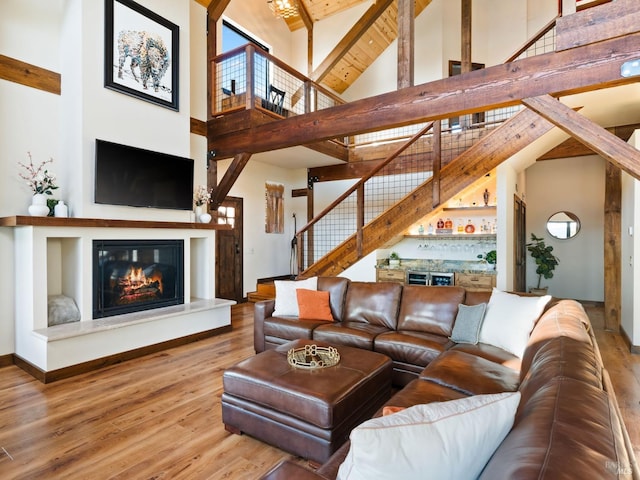 living area featuring high vaulted ceiling, a glass covered fireplace, stairway, wood finished floors, and beam ceiling