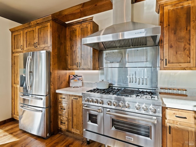 kitchen with wall chimney range hood, light countertops, brown cabinets, stainless steel appliances, and dark wood-type flooring