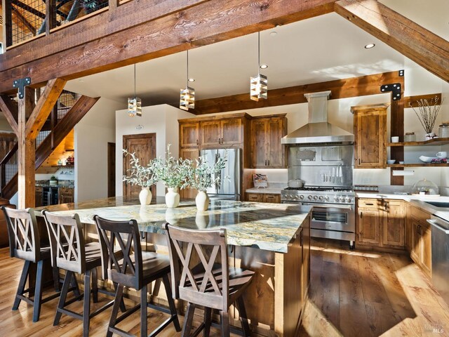 kitchen with light stone counters, a center island, wall chimney exhaust hood, appliances with stainless steel finishes, and light wood finished floors