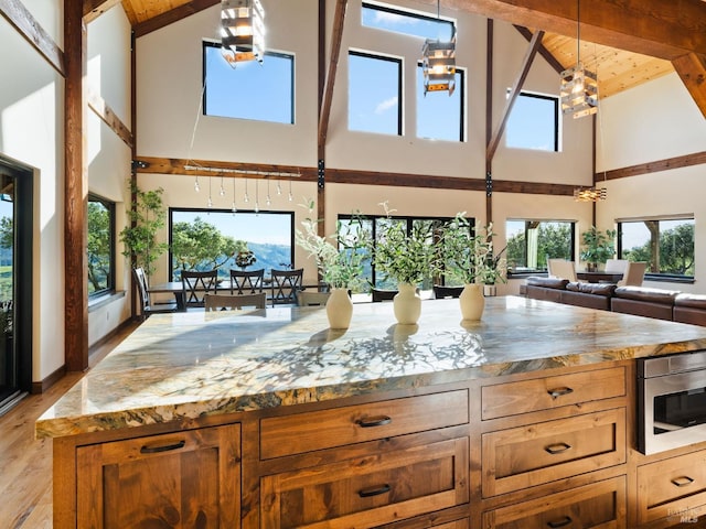 kitchen featuring high vaulted ceiling, open floor plan, light wood-style floors, and light stone counters