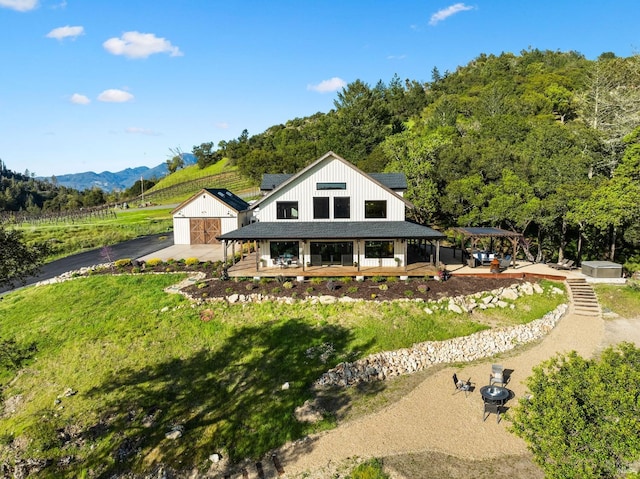 rear view of house with roof mounted solar panels, a yard, an outdoor structure, a deck with mountain view, and a shingled roof