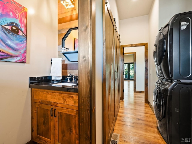 laundry room with visible vents, a barn door, a sink, light wood-type flooring, and stacked washer / dryer