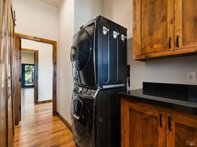 laundry area with cabinet space, baseboards, light wood finished floors, and stacked washer / drying machine