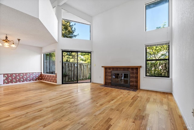 unfurnished living room featuring baseboards, wood finished floors, high vaulted ceiling, and an inviting chandelier
