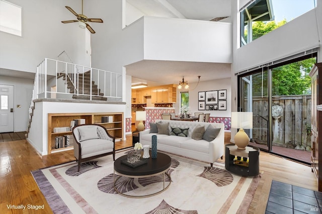 living area with ceiling fan, stairs, wood finished floors, and a towering ceiling