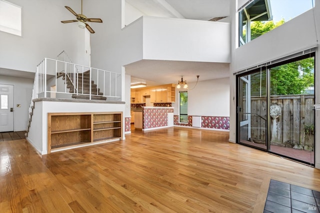 unfurnished living room with wood finished floors, a towering ceiling, stairs, and ceiling fan with notable chandelier
