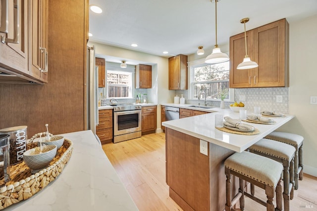 kitchen with a healthy amount of sunlight, a peninsula, brown cabinets, and appliances with stainless steel finishes