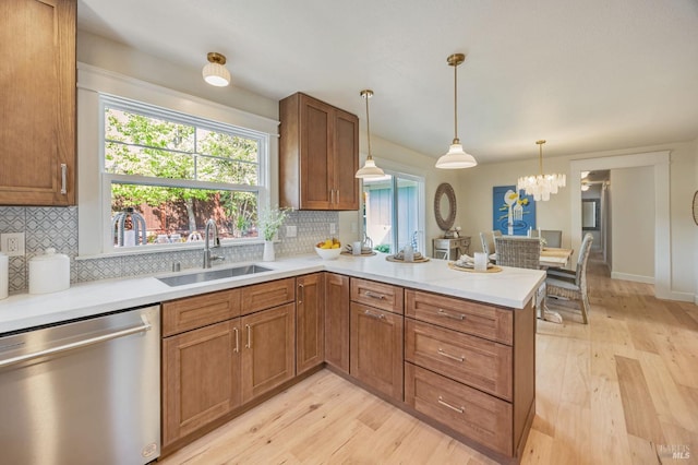 kitchen featuring light wood-type flooring, a peninsula, brown cabinets, stainless steel dishwasher, and a sink